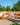 Outdoor patio set with beige sectional sofa, orange cushions, and a small table on a sunny day.