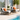 Two lounge chairs with orange cushions by a poolside, featuring a small table with a plant and fruit.