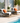 Two lounge chairs with orange cushions by a poolside, featuring a small table with a plant and fruit.