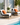 Two lounge chairs with orange cushions by a poolside, featuring a small table with a plant and fruit.