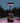 Solar lamp with pink light illuminating a small potted plant on a wooden surface at night.