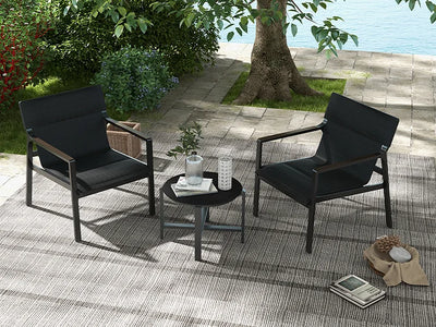 Two black chairs with a small table on a patio area with a garden and water view.