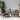 Outdoor patio set with two wicker chairs and a small table on a patio with plants and a white wall.