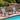 Two blue rocking chairs on a wooden deck by a pool with a stone wall and greenery in the background.