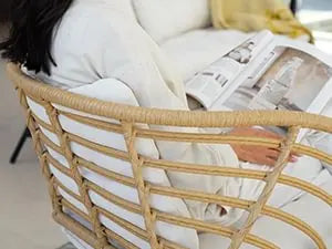 Person lying on a bed with a newspaper, wearing a white shirt and black pants, in a room with a light-colored floor.