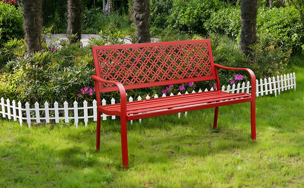 Red metal bench in a garden setting with green grass and white picket fence.