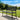 50” Metal Outdoor Bench in a park setting with trees and a clear sky.