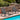 Two gray outdoor rocking chairs with a small table on a wooden deck by a pool.