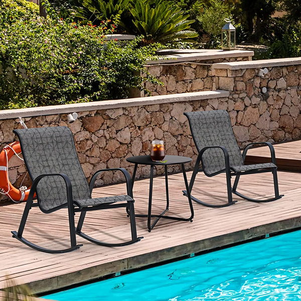 Two gray outdoor rocking chairs with a small table on a wooden deck by a pool.