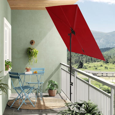 Red rectangular flat patio umbrella on a balcony with blue chairs and a small table, overlooking a green landscape.