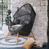 Black wicker egg chair with gray cushions, set against a stone wall and surrounded by decorative elements.