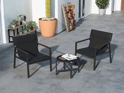 Two black outdoor chairs with a small table on a concrete patio, surrounded by potted plants.