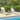 Two lounge chairs with cushions on a striped rug by a poolside with greenery in the background.