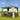 Outdoor gazebo with curtains, chairs, and a table on a grassy area with a blue sky.
