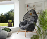Black wicker egg chair with gray cushion, set indoors near a window overlooking greenery.